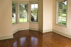 An empty room with wooden flooring and bay windows installed on the walls.
